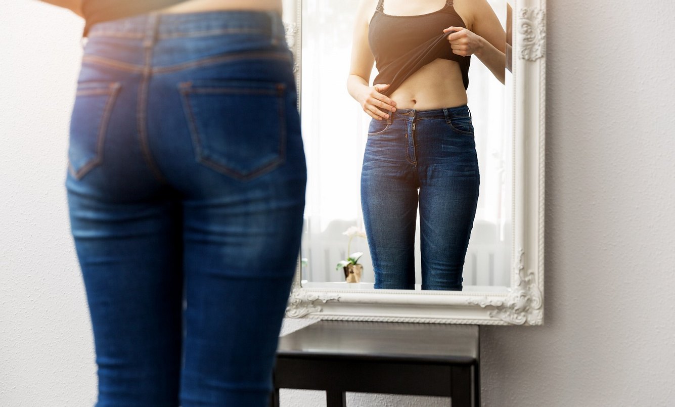 Frau untersucht ihren Bauch im Spiegel