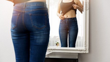 Frau untersucht ihren Bauch im Spiegel - Foto: ronstik/iStock