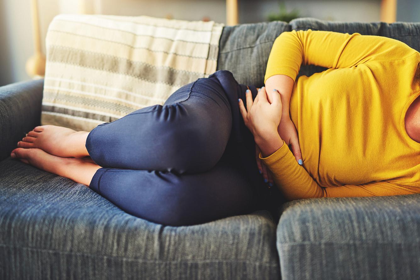 Frau mit funktionellen Bauchschmerzen liegt auf dem Sofa