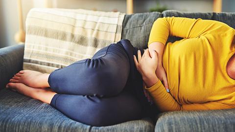 Frau mit funktionellen Bauchschmerzen liegt auf dem Sofa - Foto: iStock/Charday Penn