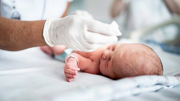 Neugeborenes Baby liegt auf einem Tuch und wird von einer Pflegekraft untersucht - Foto: iStock/fg-trade