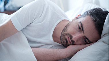 Ein Mann liegt traurig im Bett - Foto: iStock/tommaso79