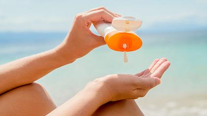 Eine Frau cremt sich am Strand mit Sonnencreme ein - Foto: iStock/ljubaphoto