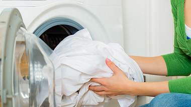 Frau packt weiße Wäsche in die Waschmaschine - Foto: iStock/ kzenon