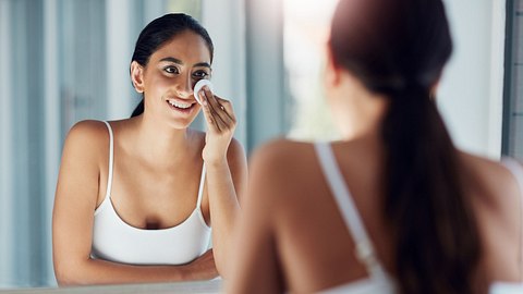 Eine Frau steht vor dem Badezimmerspiegel und reinigt ihr Gesicht mit einem Wattepad - Foto: istock_gradyreese