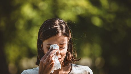 Junge Frau in der Natur hält sich Taschentuch vor die Augen wegen Heuschnupfen - Foto: iStock / RealPeopleGroup