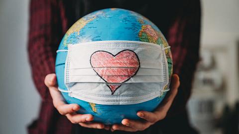 Junge Frau hält einen Globus mit einer Gesichtsmaske darauf - Foto: iStock / FilippoBacci