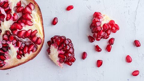 Granatapfel und einzelne Granatapfelkerne liegen auf einer auf einer weißen Unterlage - Foto: iStock/focusphotoart