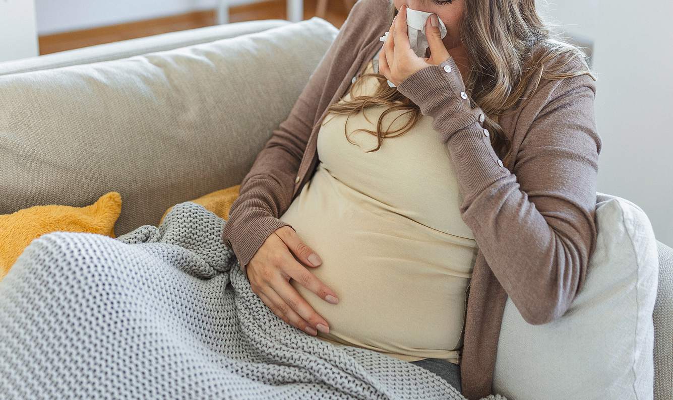 Schwangere Frau sitzt mit Decke auf dem Sofa und hat eine Grippe in der Schwangerschaft 
