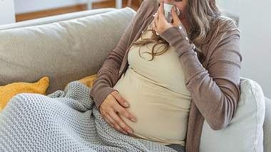 Schwangere Frau sitzt mit Decke auf dem Sofa und hat eine Grippe in der Schwangerschaft  - Foto:  iStock/stefanamer
