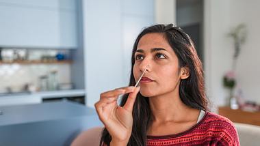 Frau nimmt bei sich selbst einen Nasenabstrich - Foto: iStock/AzmanL
