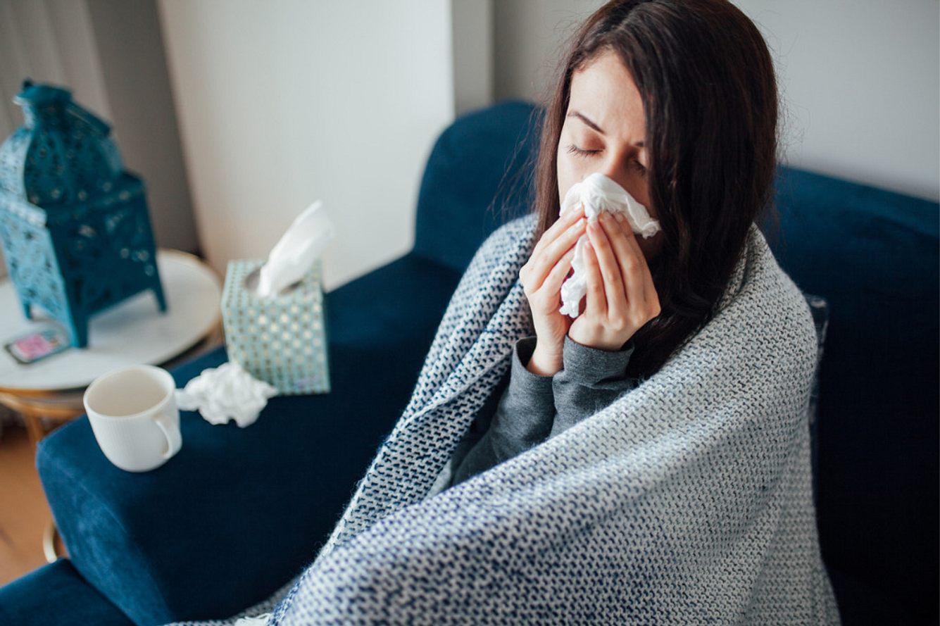 Eine Frau sitzt krank im Bett und putzt sich die Nase