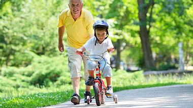 Ein kleiner Junge fährt Dreirad und sein Großvater läuft hinter ihm her - Foto: Fotolia