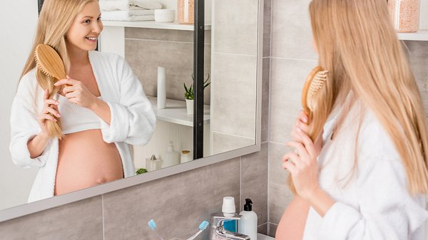 Eine schwangere Frau kämmt sich vor einem Spiegel die Haare - Foto: istock_LightFieldStudios