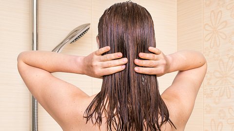 Eine Frau wäscht sich die Haare und streift mit ihren Händen durchs nasse Haar - Foto: istock_andriano_cz
