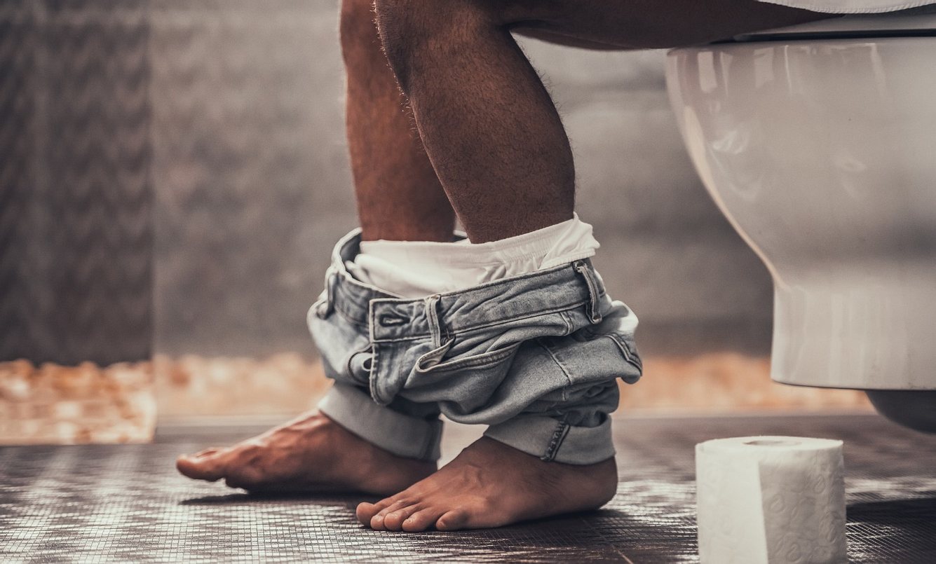 Mann sitzt auf Toilette mit Klopapier in der Hand
