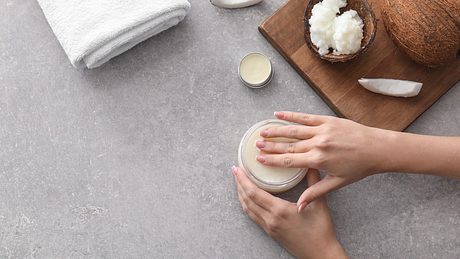 Hände liegen auf einer Creme, daneben liegt ein Handtuch sowie Kokosöl und Stücke einer Kokosnuss - Foto: istock_serezniy
