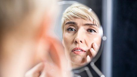 Eine Frau betrachtet ihre Falten im Spiegel - Foto: iStock/Prostock-Studio