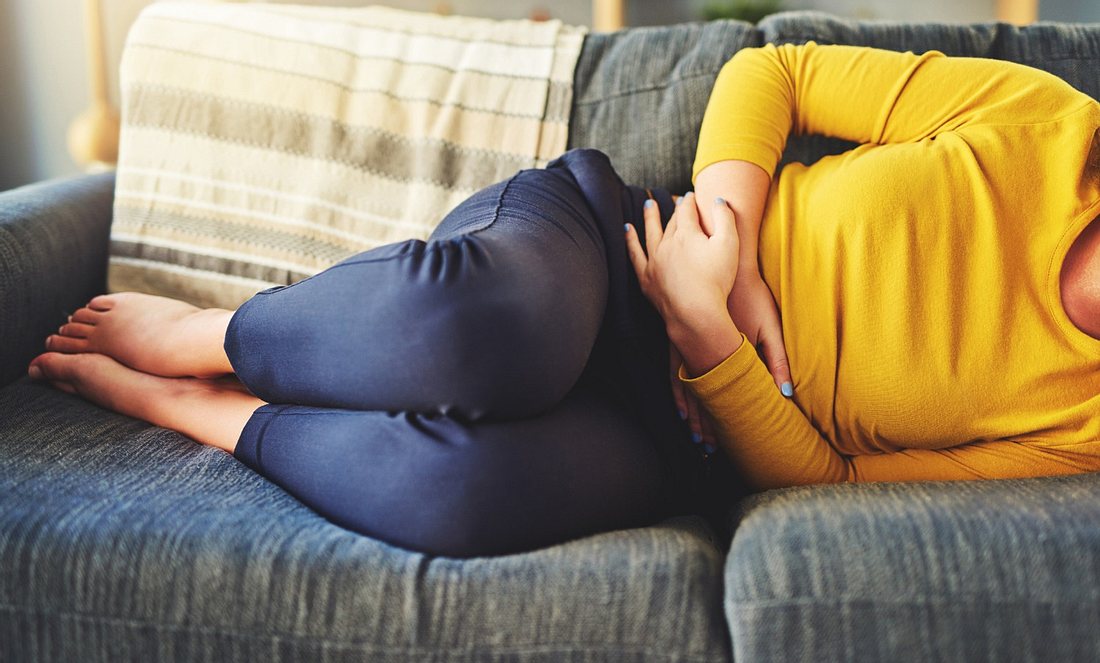 Eine Frau liegt mit Bauchschmerzen auf dem Sofa