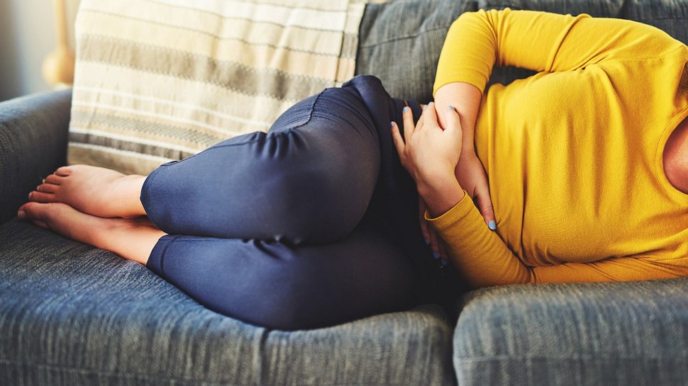 Eine Frau liegt mit Bauchschmerzen auf dem Sofa - Foto: istock_Charday Penn