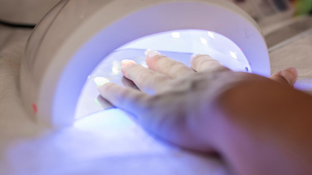 Frau hält Hand unter UV-Lampe im Nagelstudio - Foto: iStock/StockPlanets