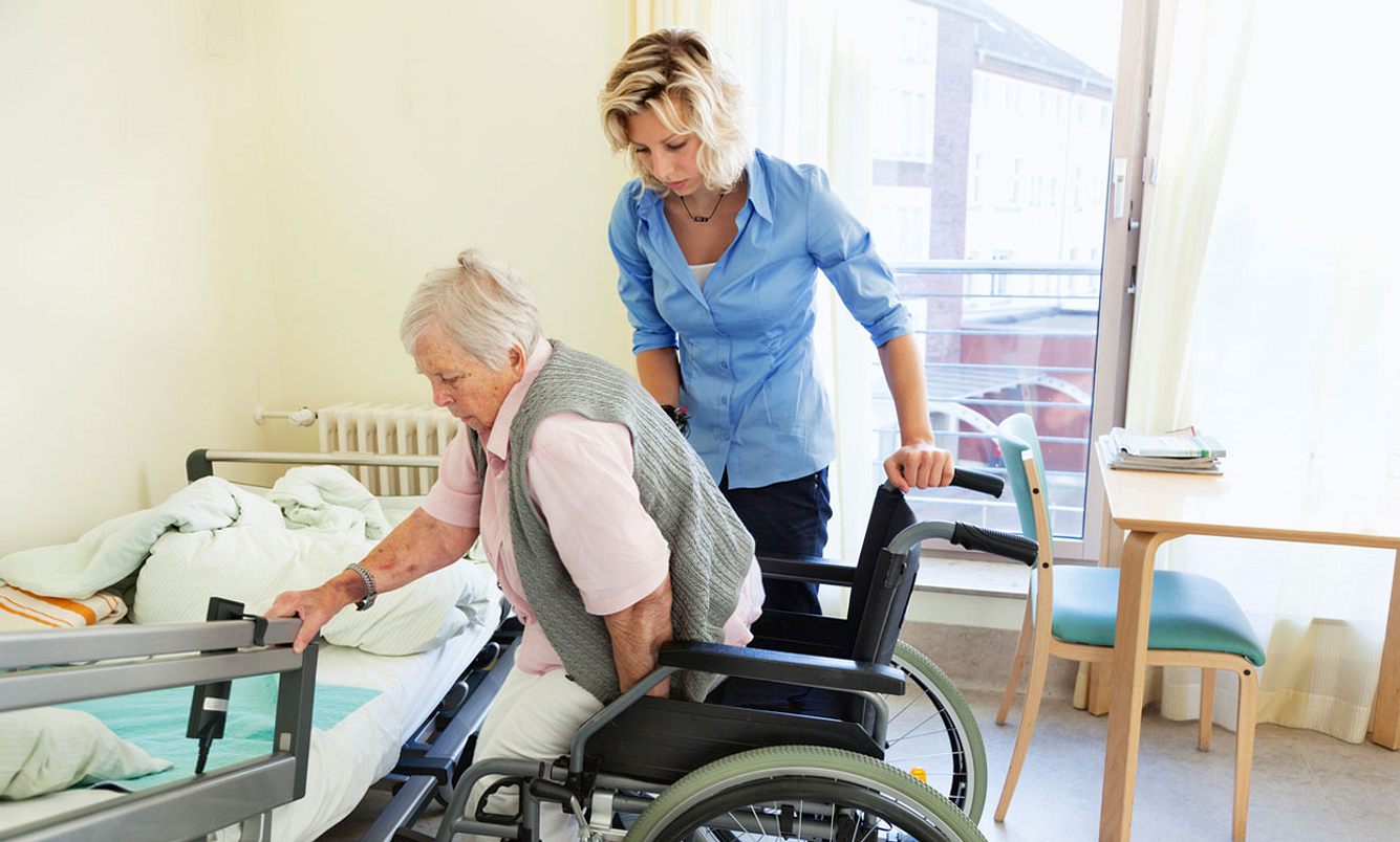 Eine Pflegerin hilft eine Seniorin aus dem Rollstuhl