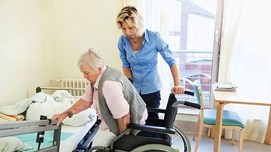 Eine Pflegerin hilft eine Seniorin aus dem Rollstuhl - Foto: SilviaJansen/iStock