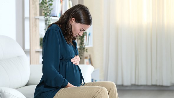 Eine Schwangere hält ihren Bauch und hat Schmerzen - Foto: iStock/AntonioGuillem
