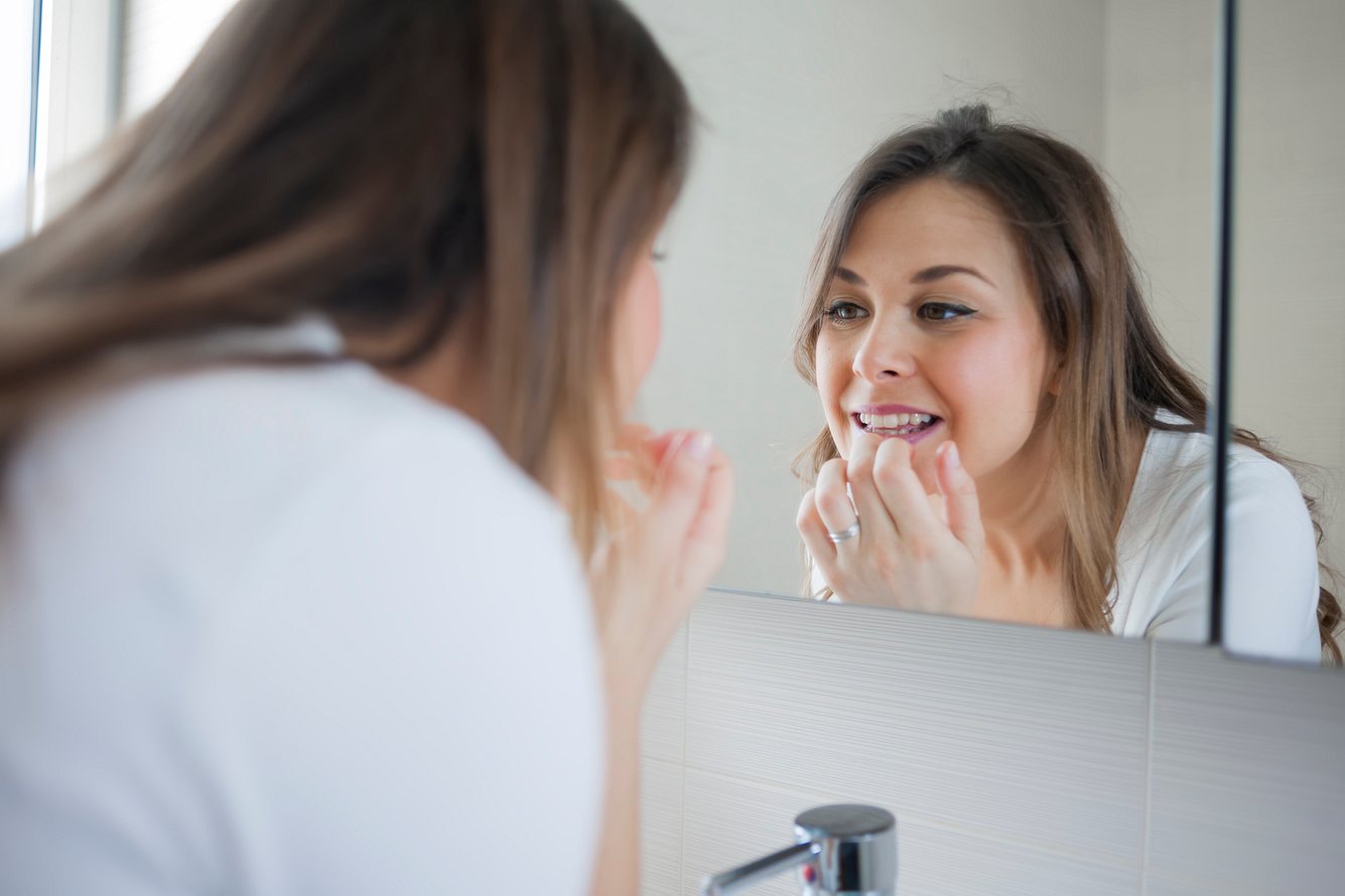 Eine Frau schaut sich ihre Zähne im Spiegel an