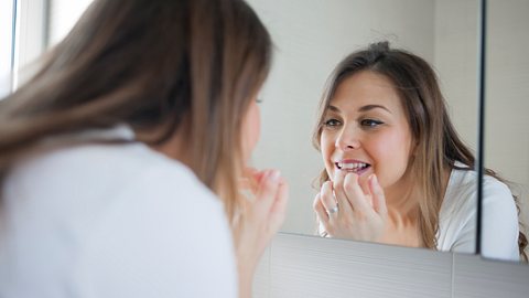 Eine Frau schaut sich ihre Zähne im Spiegel an - Foto: iStock/Vesna Andjic