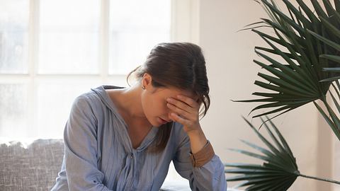 Eine Frau sitzt auf erschöpft auf dem Sofa - Foto: iStock/fizkes