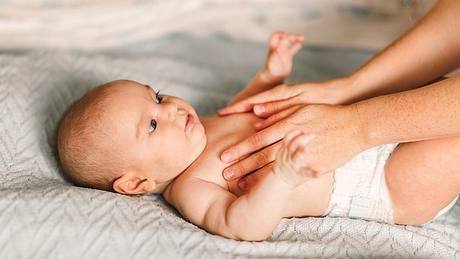Person fasst Baby in Windeln am Bauch - Foto: iStock/Polina Strelkova