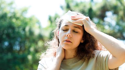 Junge Frau sitzt erschöpft in der Sonne und hält sich ein Tuch an die Stirn - Foto: iStock/eternalcreative