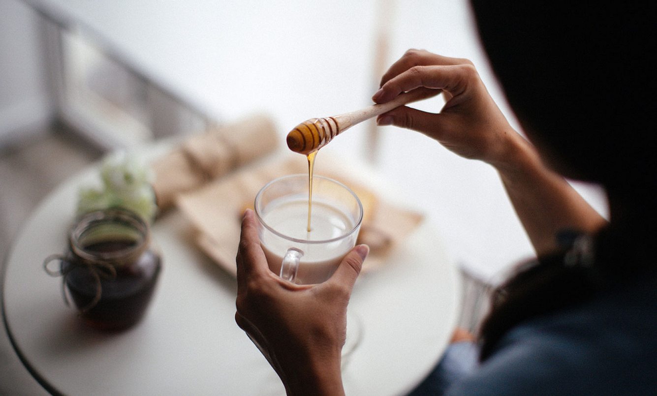 Frau lässt Honig in eine Tasse Milch fliessen