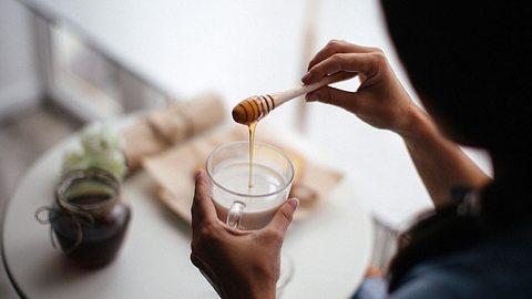Frau lässt Honig in eine Tasse Milch fliessen - Foto: iStock/StefaNikolic