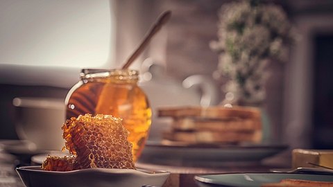 Ein Glas mit Honig, vor dem eine Bienenwabe liegt - Foto: istock_GMVozd