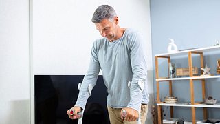 Ein Mann im mittleren Alter läuft auf Krücken in seinem Wohnzimmer - Foto: iStock/AndreyPopov