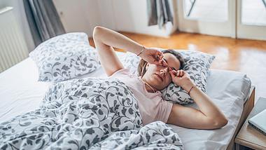 Eine Frau liegt morgens im Bett und reibt sich die Augen - Foto: iStock/Hirurg