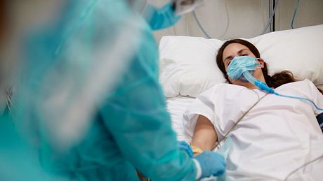 Frau liegt im Krankenbett und wird beatmet, Ärztin in Schutzkleidung prüft Tropfnadel - Foto: iStock/Tempura 