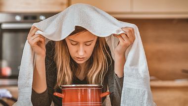 Eine Frau inhaliert über einem Kochtopf - Foto: iStock/ljubaphoto
