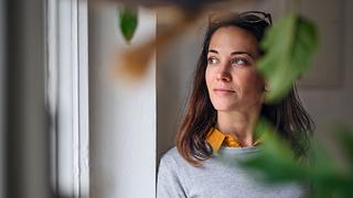 Frau schaut entspannt aus dem Fenster und ist innerlich ruhig - Foto: iStock/Halfpoint