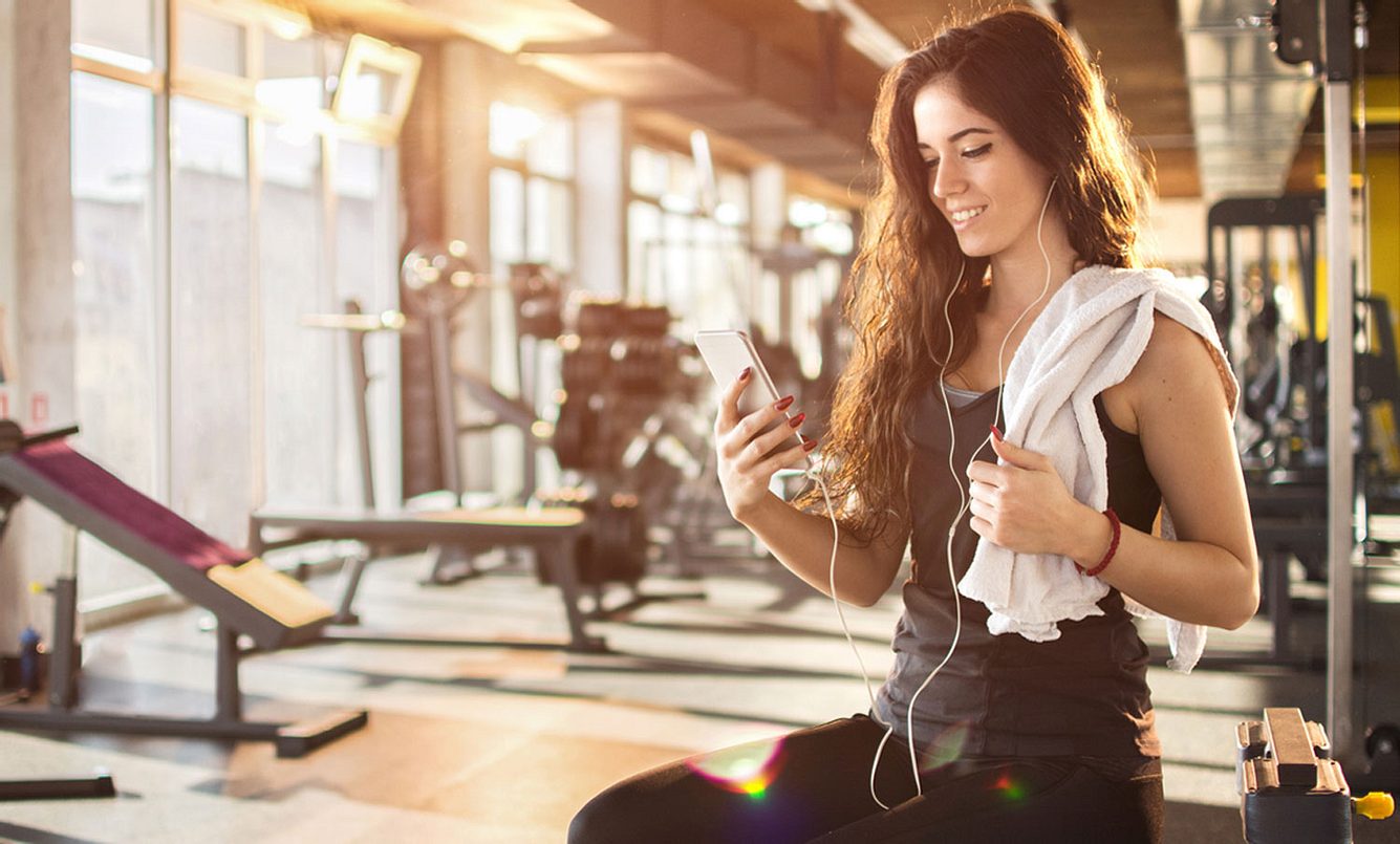 Junge Frau sitzt mit Handy im Fitnessstudio