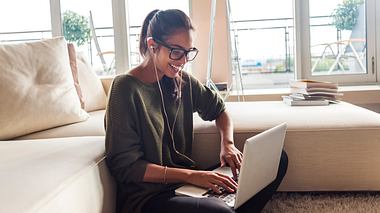 Eine Frau mit Brille arbeitet am Laptop und lacht - Foto: iStock/DaniloAndjus