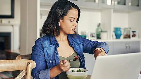 Eine Frau isst einen Salat und schaut dabei auf die Uhr - Foto: istock_mapodile