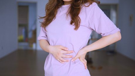 Eine Frau hält sich den Bauch und die Flanke - Foto: iStock/shih-wei