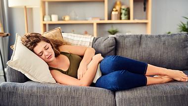 Sorbitintoleranz: Junge Frau liegt mit Bauchschmerzen auf dem Sofa - Foto: iStock-1150013526 Charday Penn