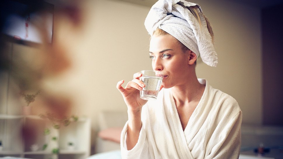 Junge Frau im Bademantel trinkt ein Glas Wasser - Foto: iStock/liderina