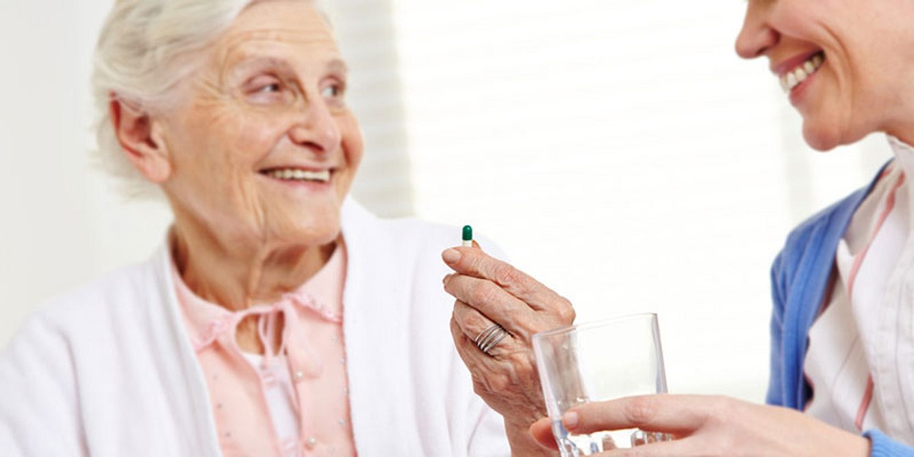 Eine junge Frau gibt einer alten Frau eine Tablette
