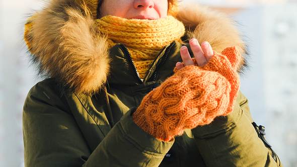 Eine Frau zieht sich draußen Handschuhe an - Foto: iStock/invizbk