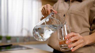 Eine Frau füllt Wasser aus einer Karaffe ins Glas - Foto: iStock_Andrii Borodai